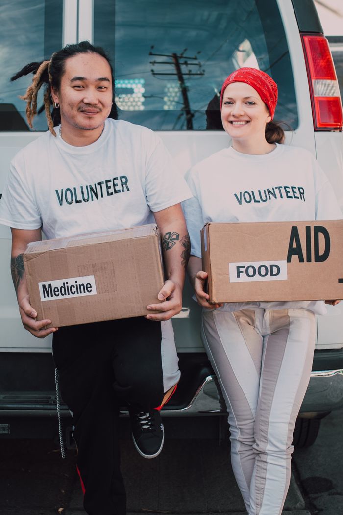 gallery-img-05 Two volunteers holding aid boxes with medicine and food labels, supporting charity causes.