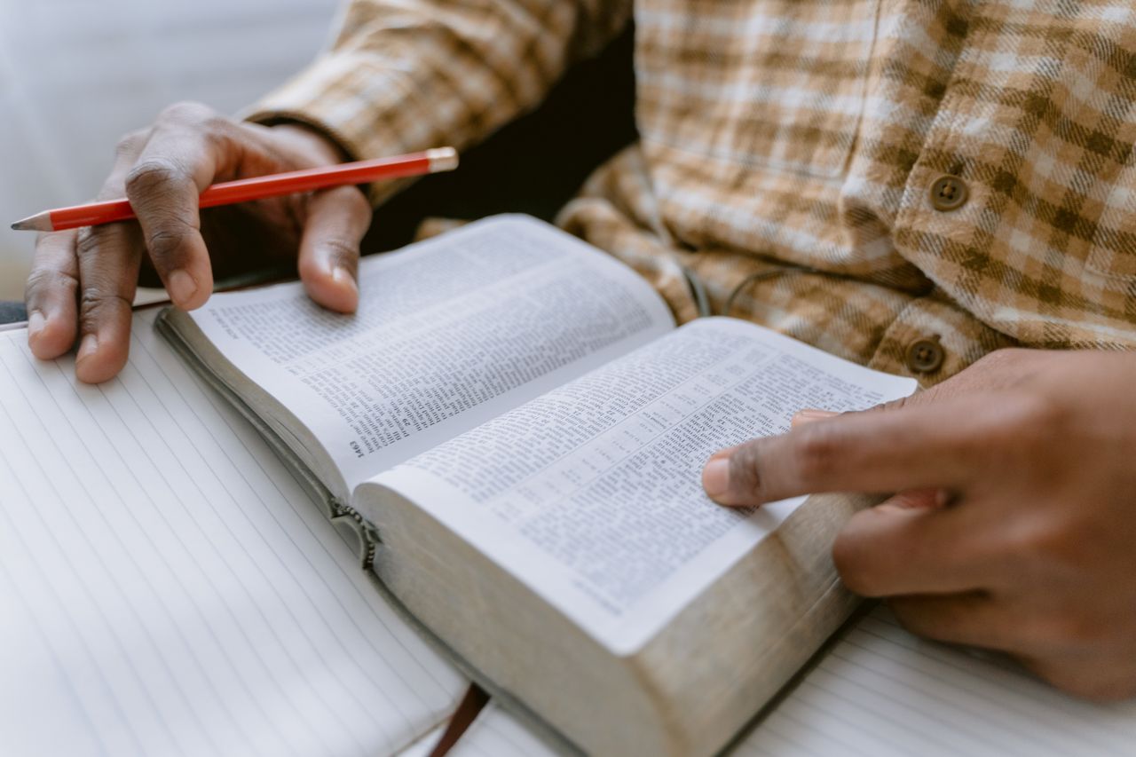 hero-gallery-01 Hands holding an open Bible while taking notes with a pencil.